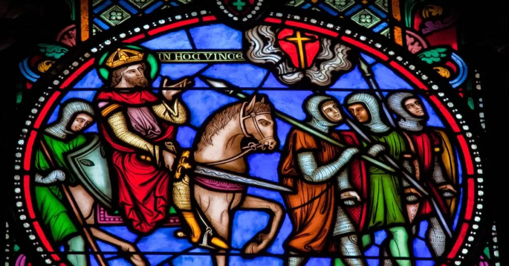 A stained glass window of crusaders on their way to Jerusalem during the First Crusade in the 11th century. The leftmost figure is wearing a green tabard. He carries a pike and a shield. The second figure is mounted on a horse, wears a crown, and is armed with a sword. Three other soldiers wearing tabards and carrying pikes and spears march in front of the mounted figure.